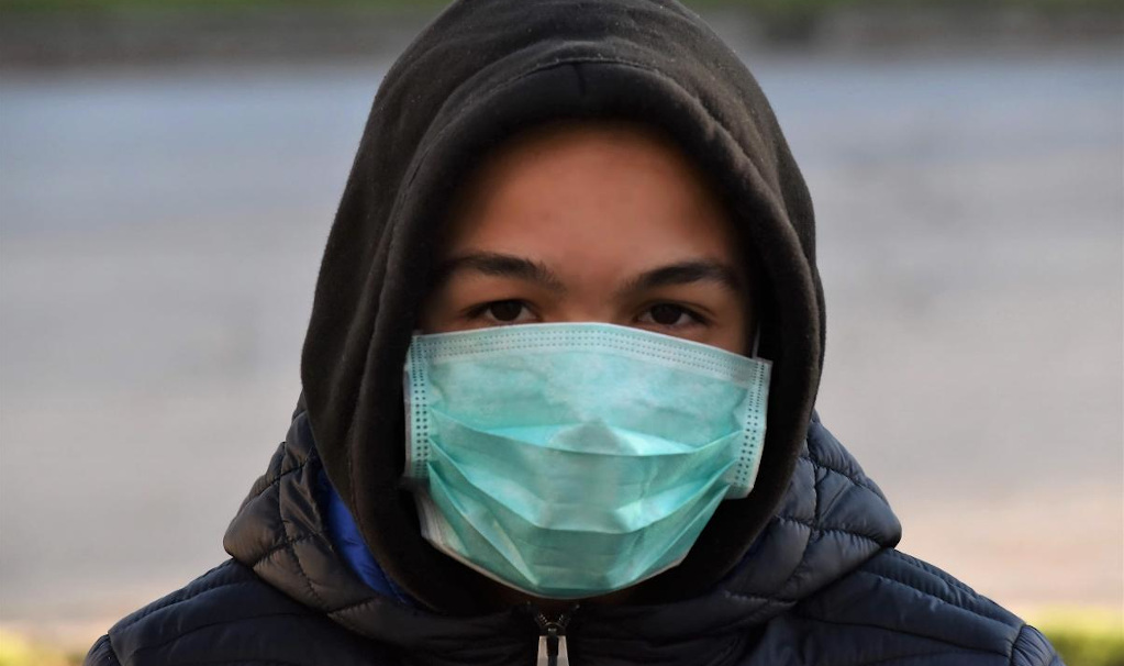 A young person wearing a hoodie and a surgical mask