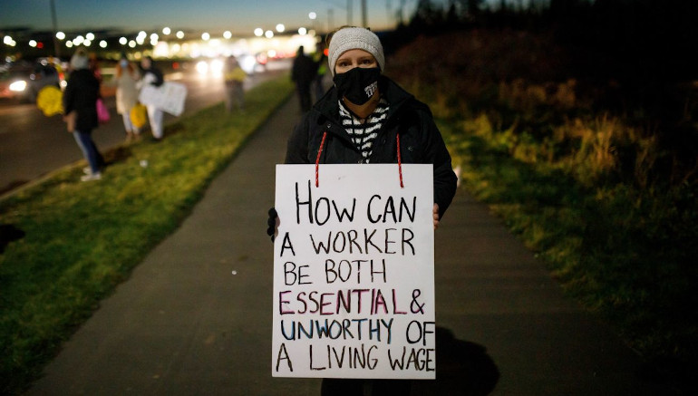 A member of Canadian Union of Public Empleyees holding a sign which says. "How can a worker be both essential and unworthy of a living wage?"